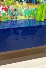 Blaues NOVUS Sideboard mit glänzender Oberfläche vor künstlerischer Wand, präsentiert bei Möbel Zeppenfeld in Olpe - Foto Möbel Zeppenfeld