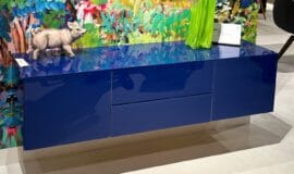NOVUS von Scholtissek bei Zeppenfeld Blaues NOVUS Sideboard mit glänzender Oberfläche vor künstlerischer Wand, präsentiert bei Möbel Zeppenfeld in Olpe - Foto Möbel Zeppenfeld